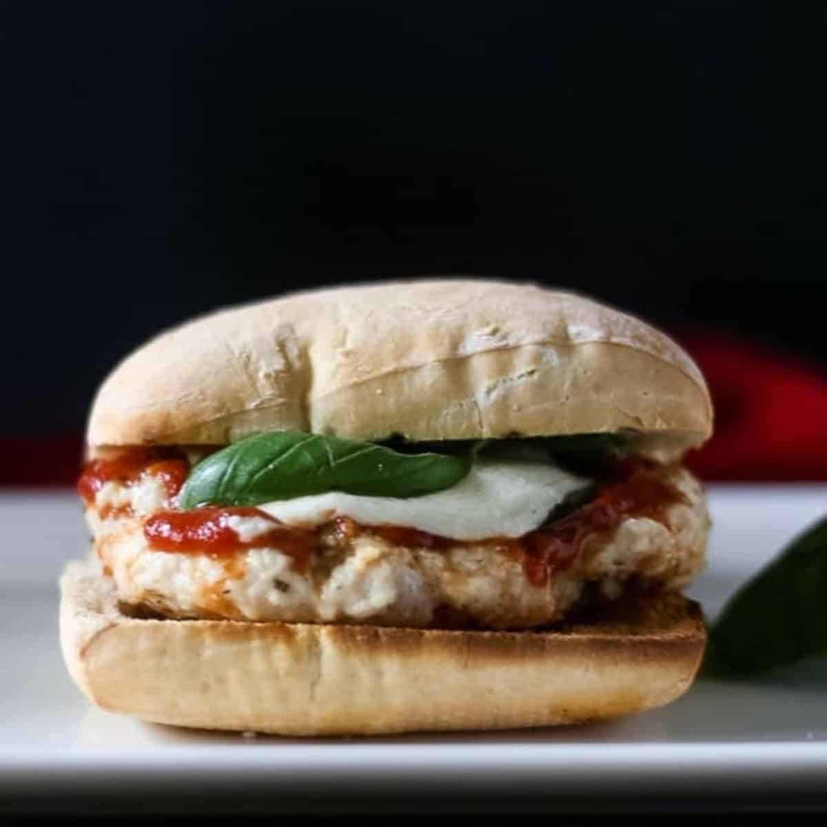 A side view of a ciabatta roll with a chicken parm patty on it.