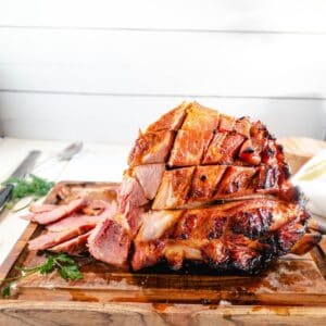 A cooked honey glazed ham on a wooden cutting board.