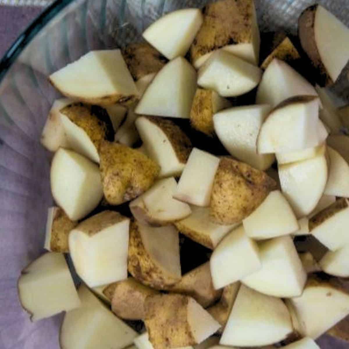 A glass bowl of raw potatoes cut into pieces to be roasted.