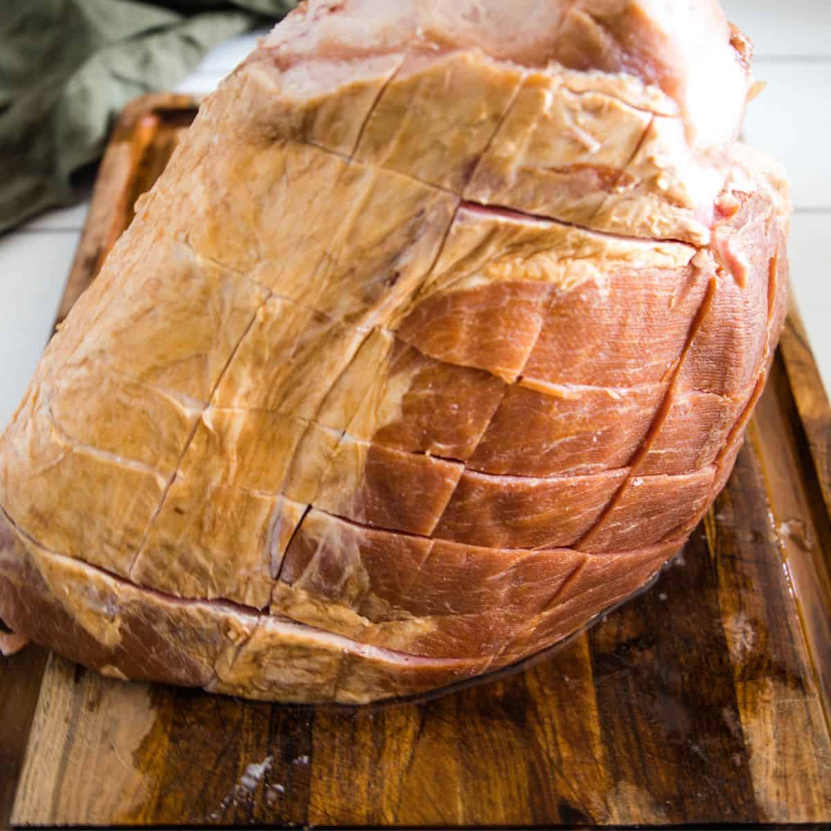 A smoked ham that has been scored and getting ready to be placed in the oven.