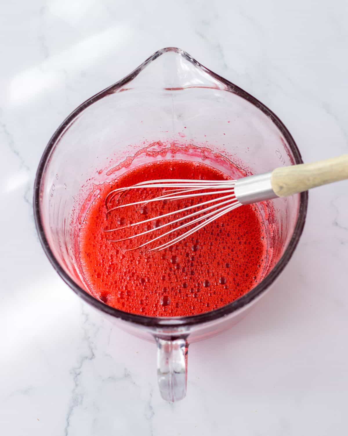 A glass bowl with strawberry gelatin combined with boiling water for a strawberry no bake pie with a pretzel crust. 