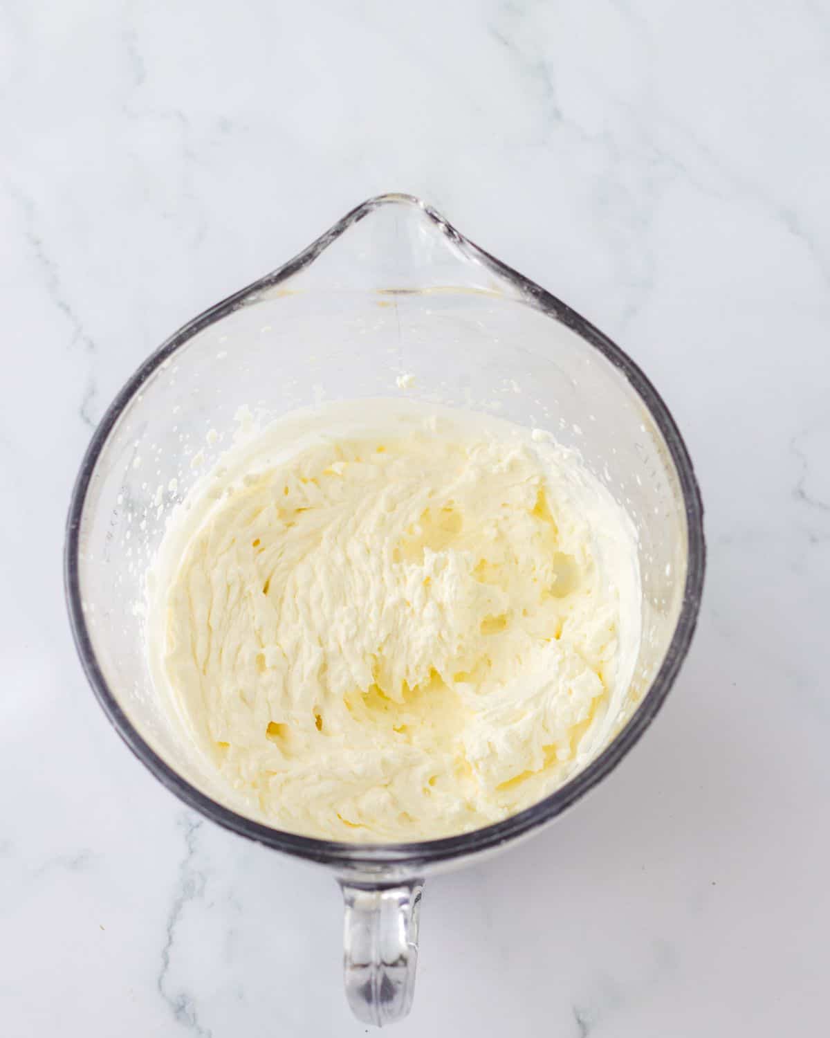 A glass measuring bowl with whipped cream that has been whipped to stiff peaks to make no-bake strawberry pie. 