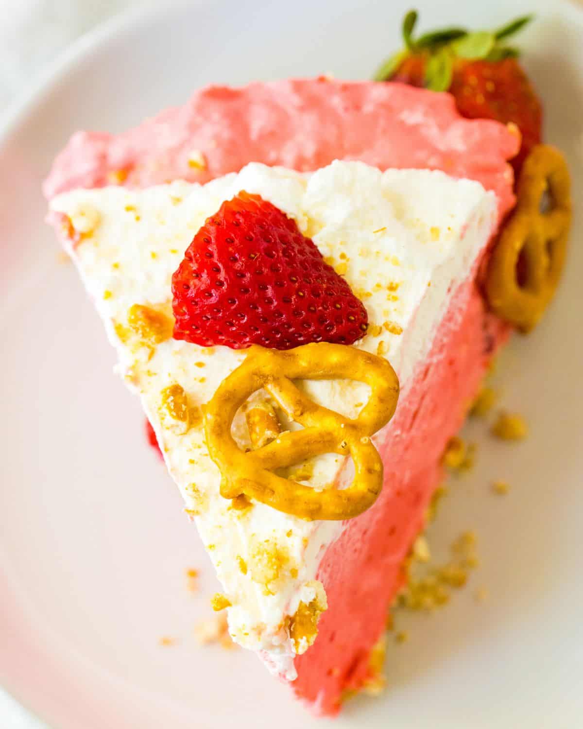 A slice of no bake strawberry pretzel pie topped with a slice of strawberry and a pretzel as garnish.