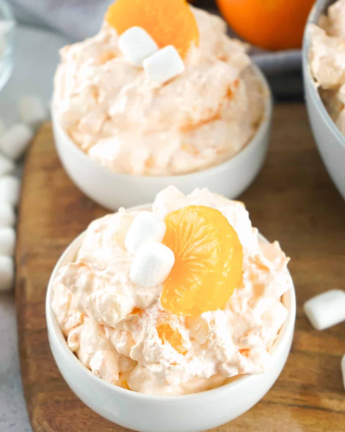 An orange fluff salad in a bowl topped with an orange slice and marshmallows.