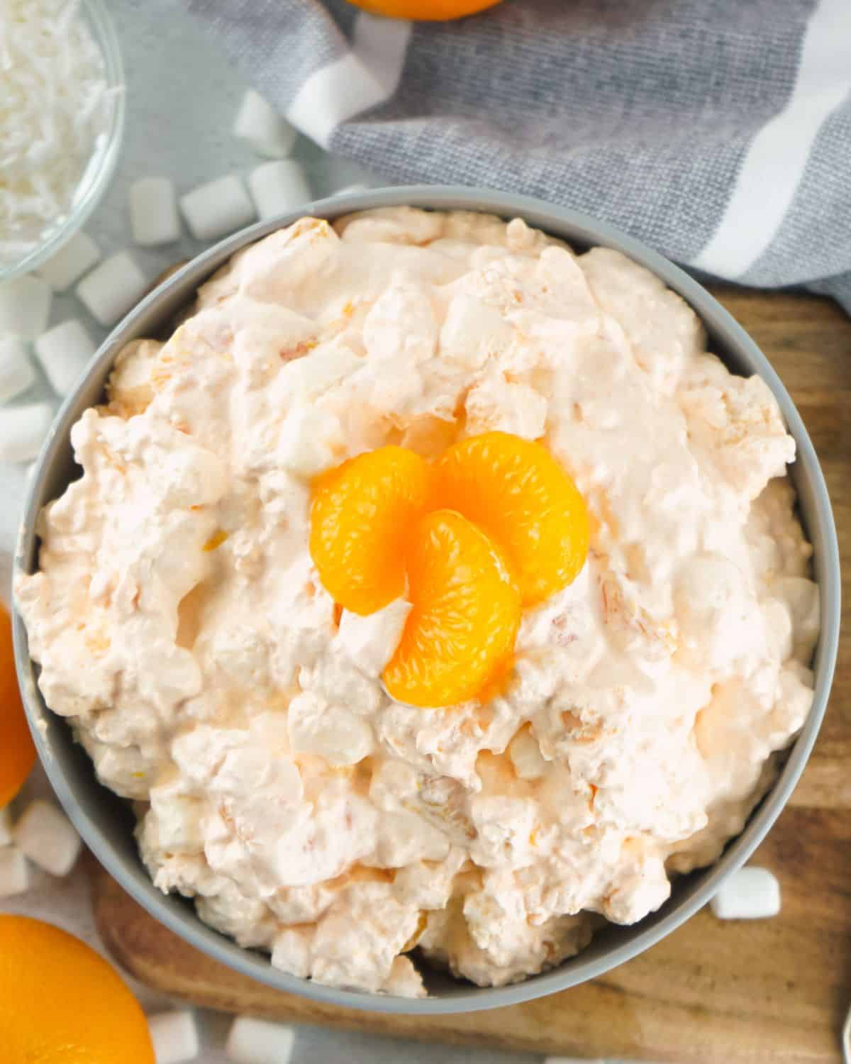 An orange fluff recipe in a bowl topped with mandarin orange slices and marshmallows.