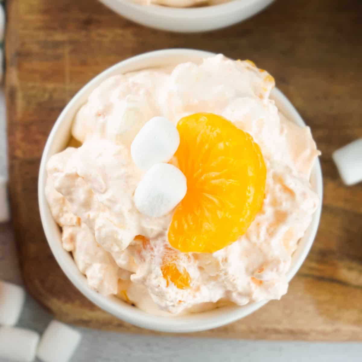 Orange fluff salad in a bowl with a slice of mandarin orange and marshmallows on top for garnish.