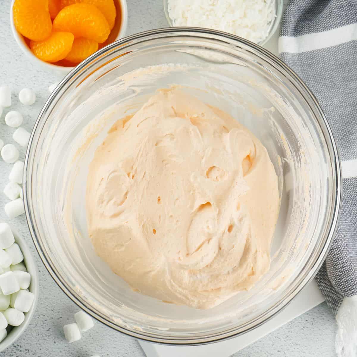 A glass bowl with cool whip and orange gelatin powder mixed together.