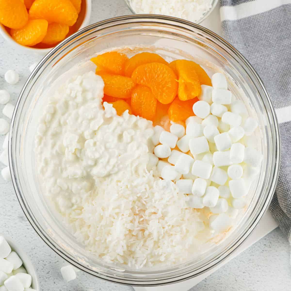 A glass bowl with mandarin oranges, mini marshmallows and orange flavored cool whip to make an orange salad with cottage cheese. 