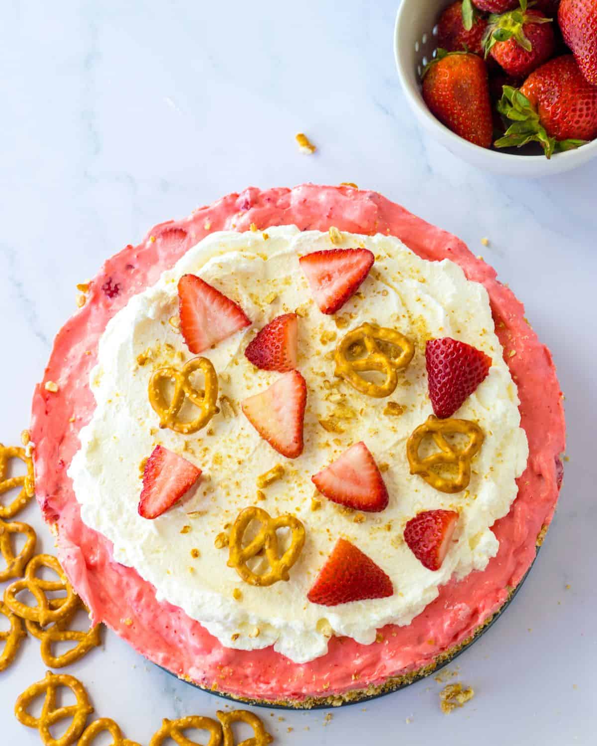 An overhead view of a no bake strawberry pie topped with strawberries and pretzels.