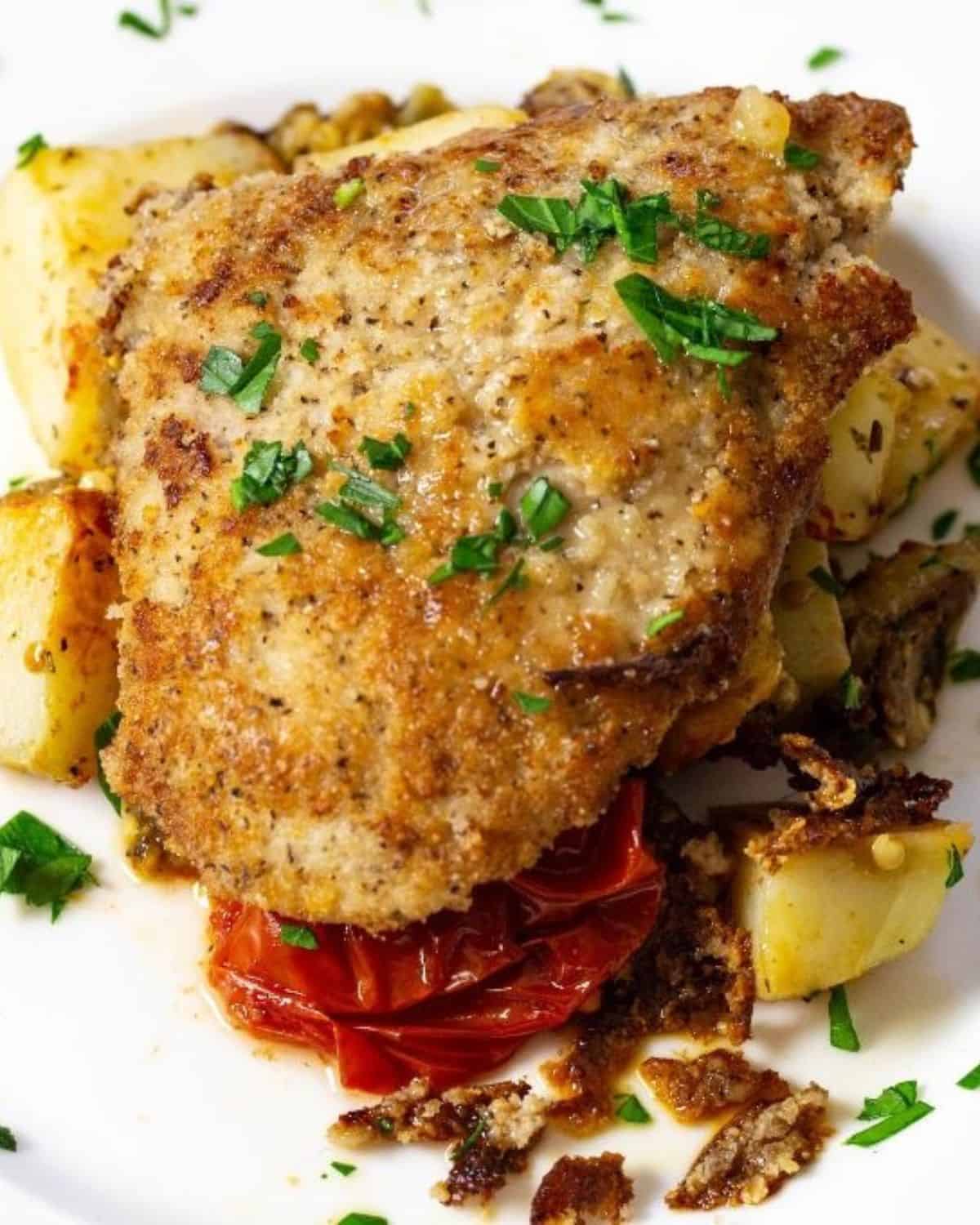 Roasted veggies topped with sauteed veal cutlets on a white plate topped with a white wine sauce.