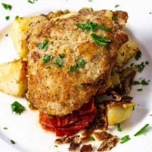 A layer of Mediterranean vegetables are topped with a breaded and fried veal cutler.