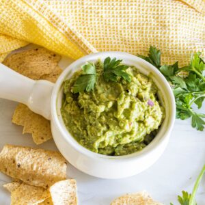 A bowl of homemade guacamole in a bowl topped with cilantro.