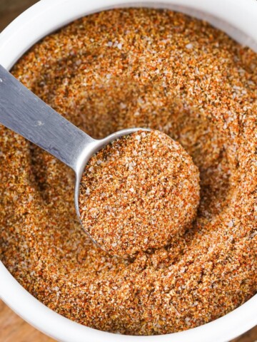Fajita seasoning spice mix in a white bowl with a measuring spoon in it.