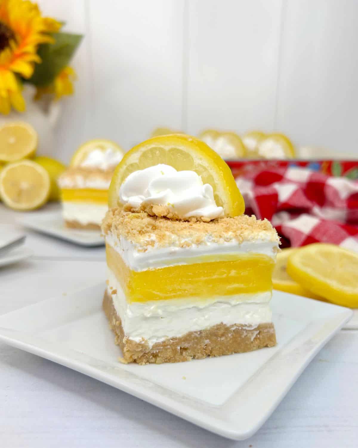 A layered lemon lush lasagna topped with graham grackers, whipped cream, and a lemon wedge.