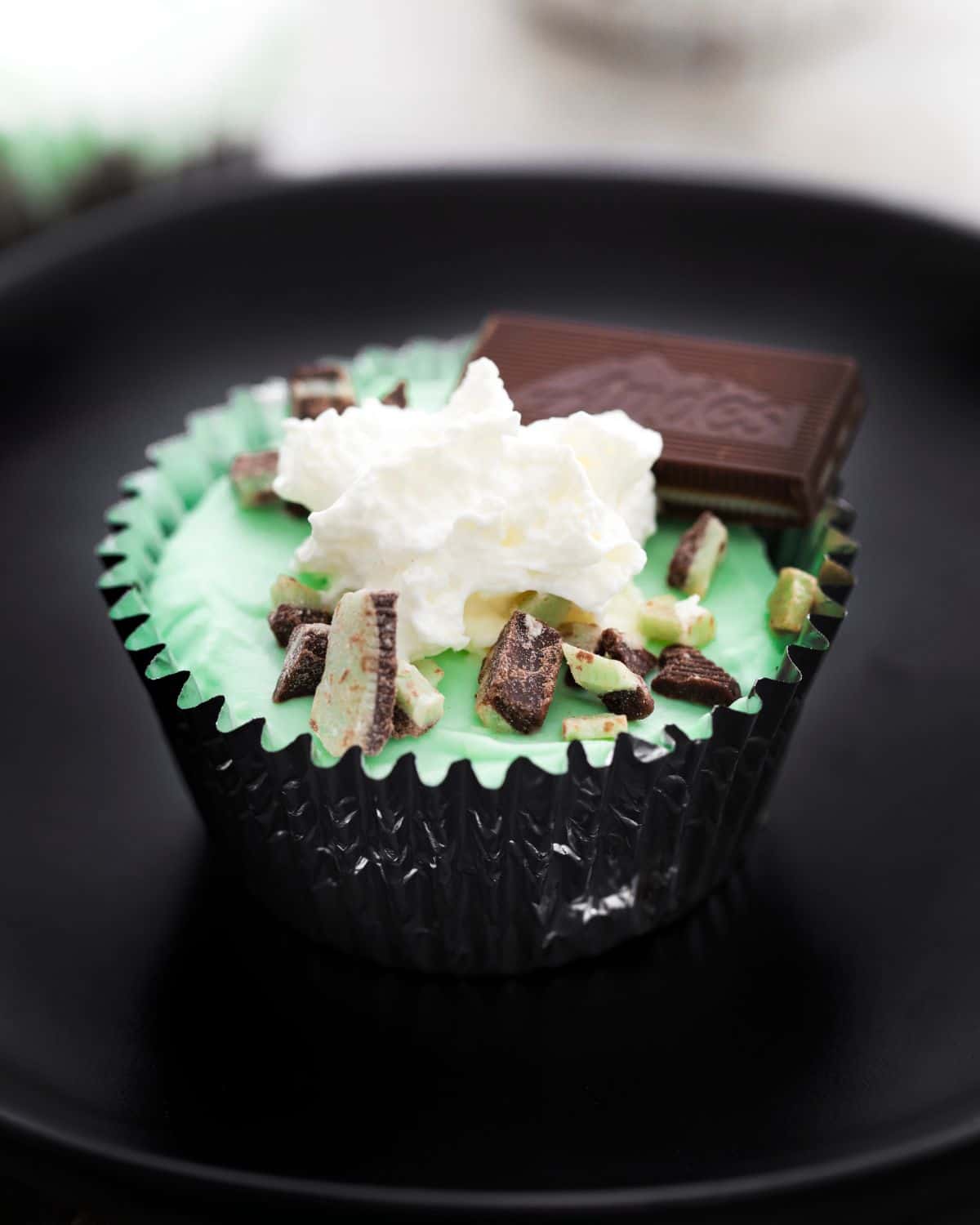 Grasshopper mini cheesecake cups topped with whipped cream and chopped mint candy.