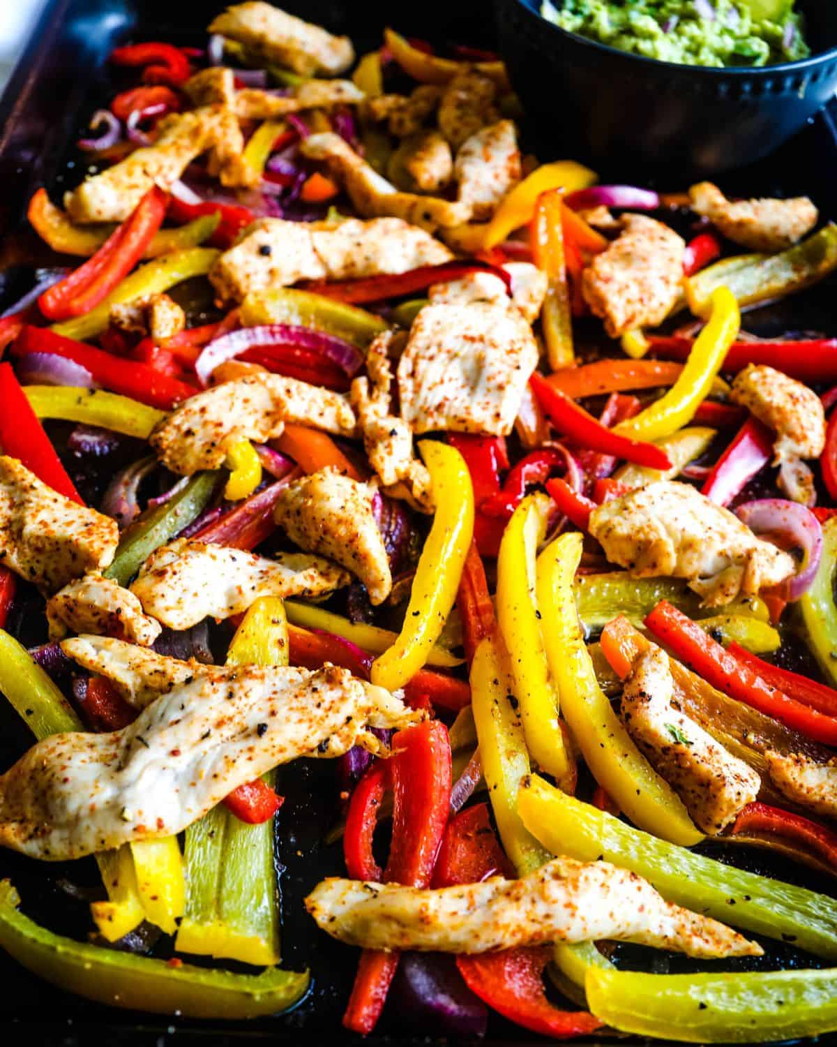 A large sheet pan with sliced peppers and chicken to make fajitas.