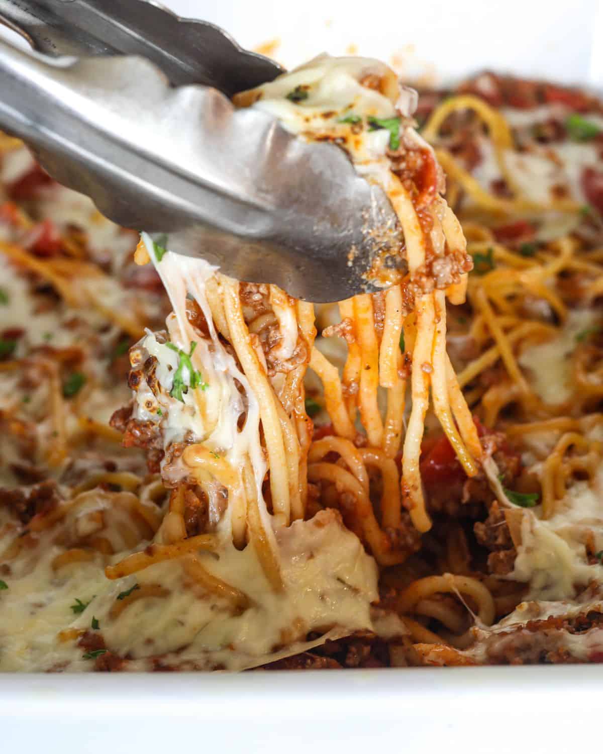 Baked spaghetti with cheese being picked up from a casserole dish.