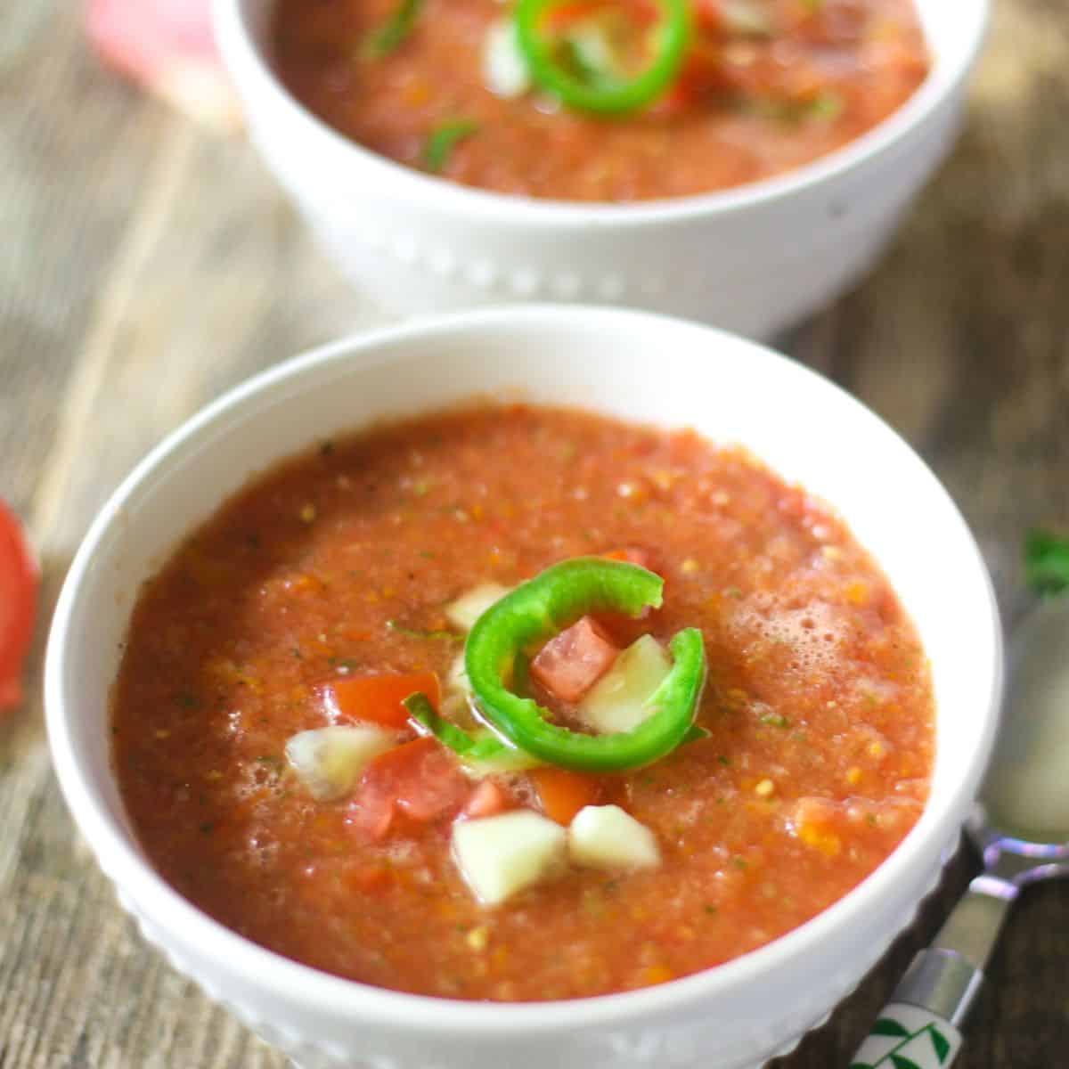 A bowl of gazpacho topped with jalapeno, tomatoes, and cucumbers.
