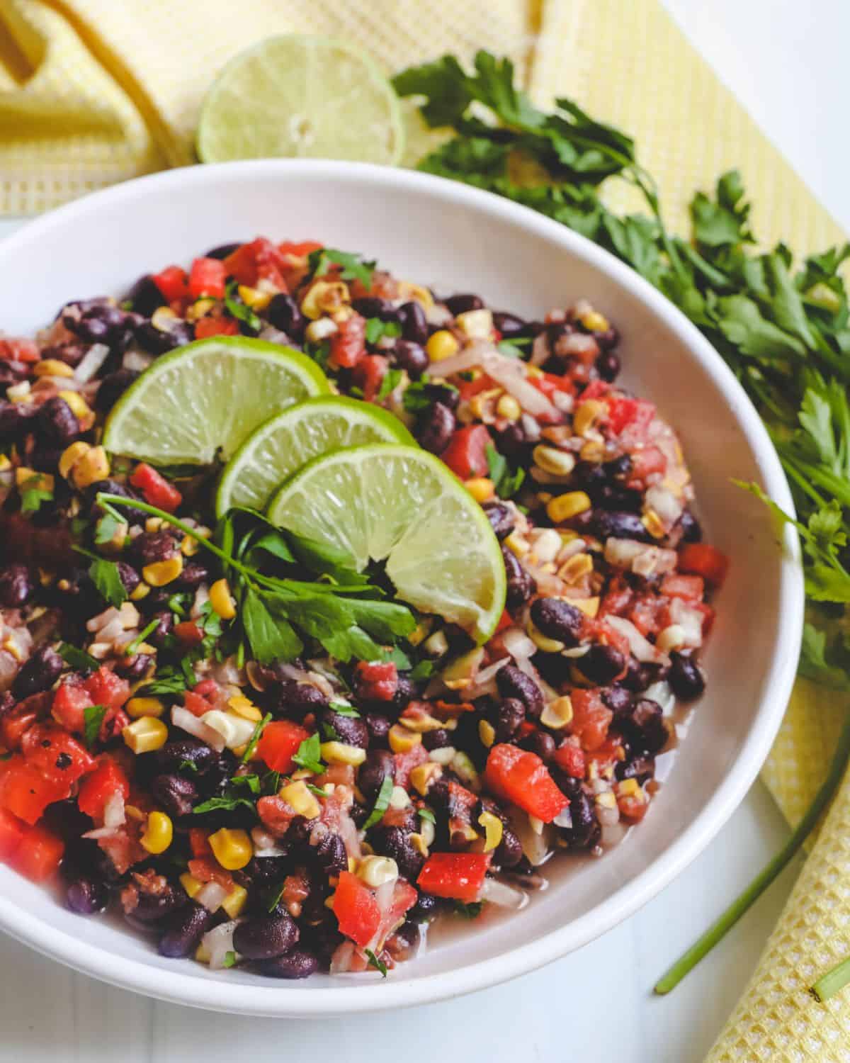 A white bowl filled with black beans, tomatoes, corn, and jalepeno to make a Black Bean Salad.