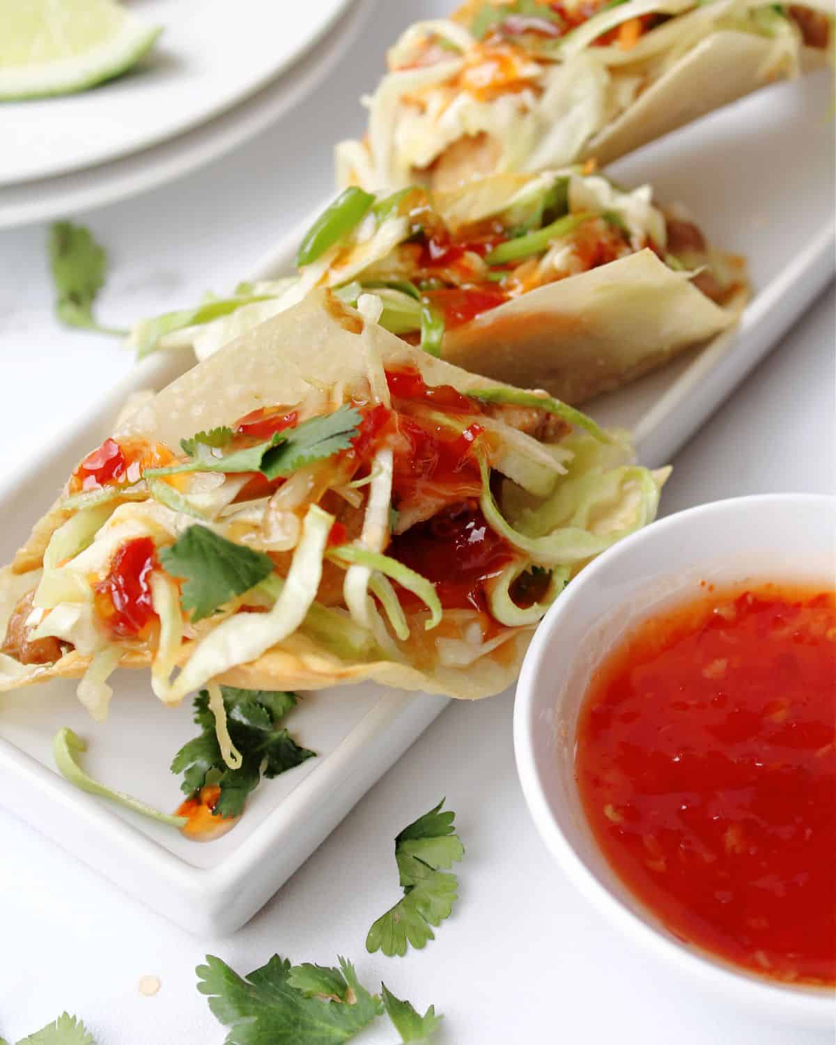 Wonton tacos with chicken and coleslaw and a dipping sauce on the side.