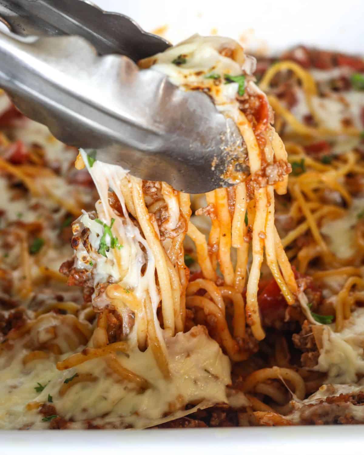 Spaghetti in marinara sauce being picked up from a casserole dish.