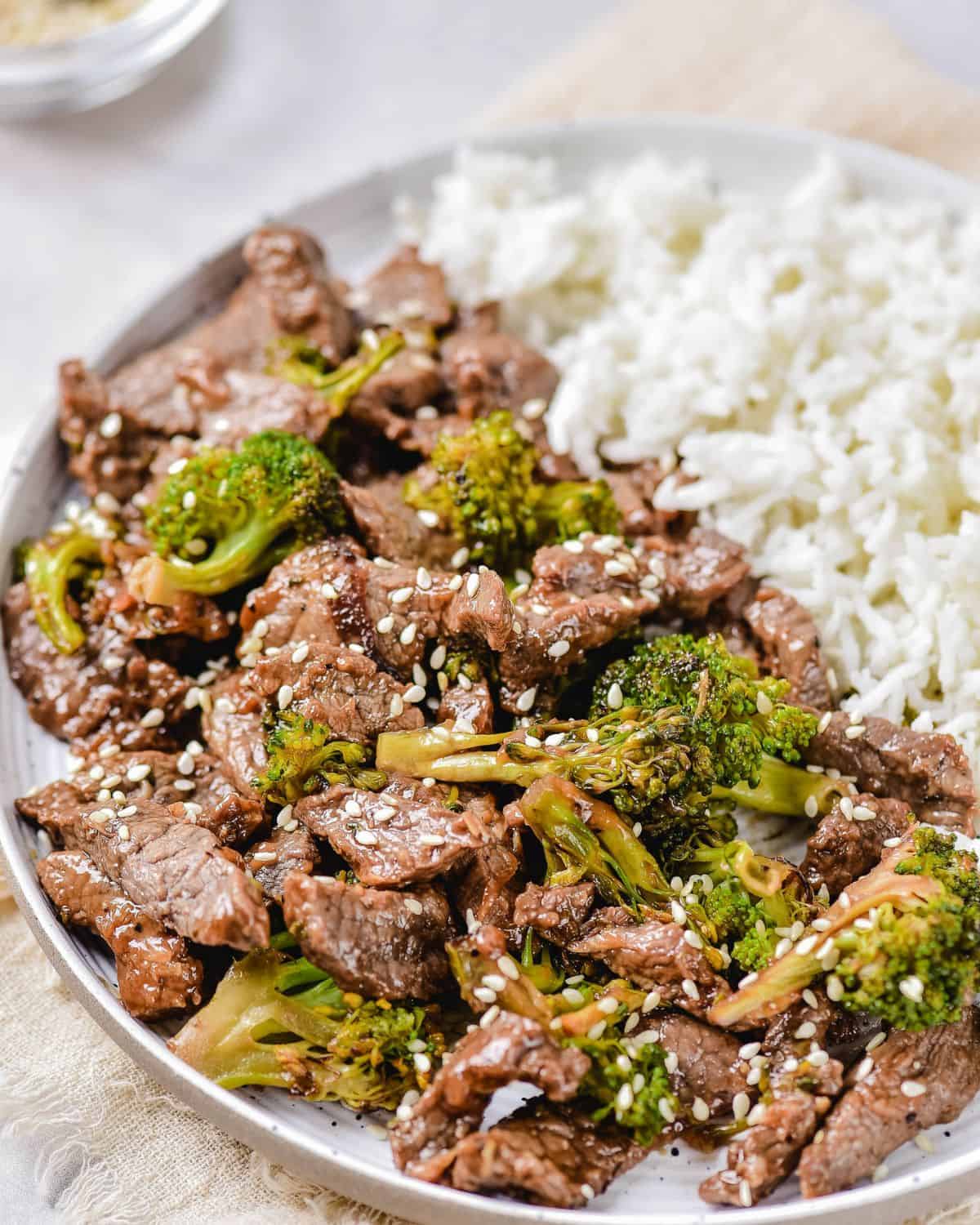 A white bowl with stir fry beef and broccoli topped with sesame seeds. 