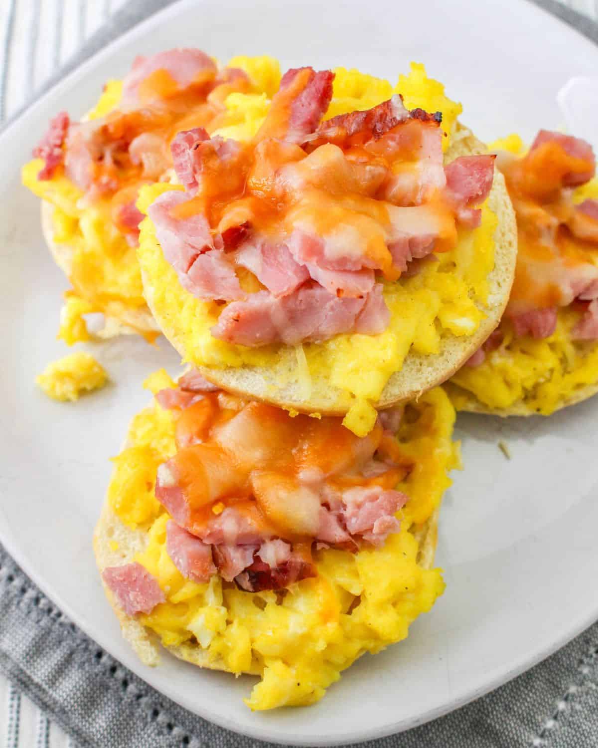 A plate with pizza breakfast bagels topped with eggs, ham, and cheese.