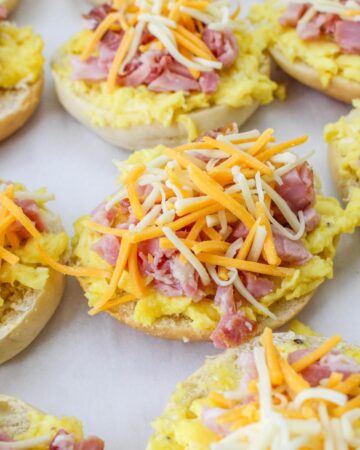 Shredded cheese and diced ham on egg pizza bagels, process shots.
