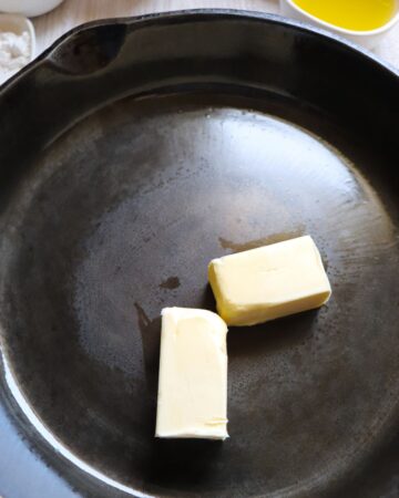 A cast iron pan with butter melting to make the base for a pineapple upside down cake. 