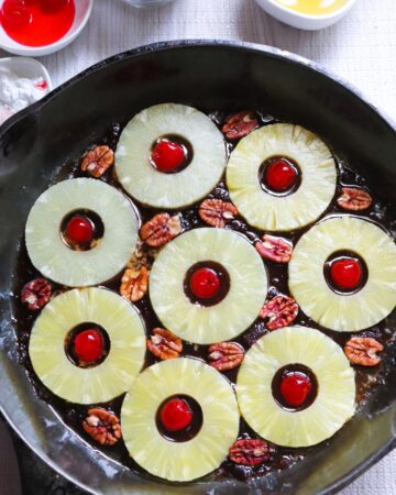 A cast iron pan with pineapple slices and maraschino cherries for a pineapple upside down cake.