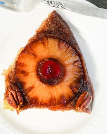 A slice of upside down cake with pineapples and cherries. 