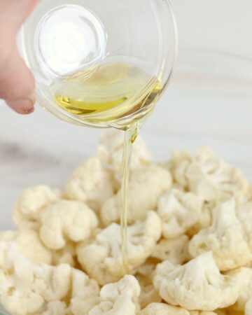 Olive oil, salt, and pepper being poured on cauliflower.