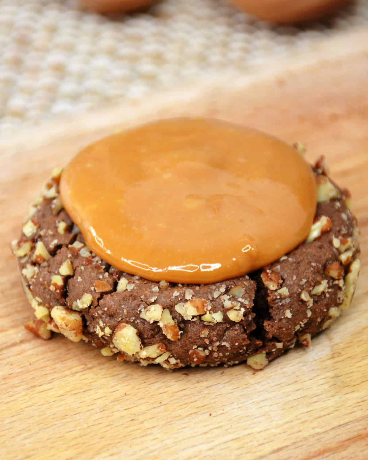 A copycat chocolate crumbl turtle cooklie with a caramel swirl on top of the cookie as a process shot.