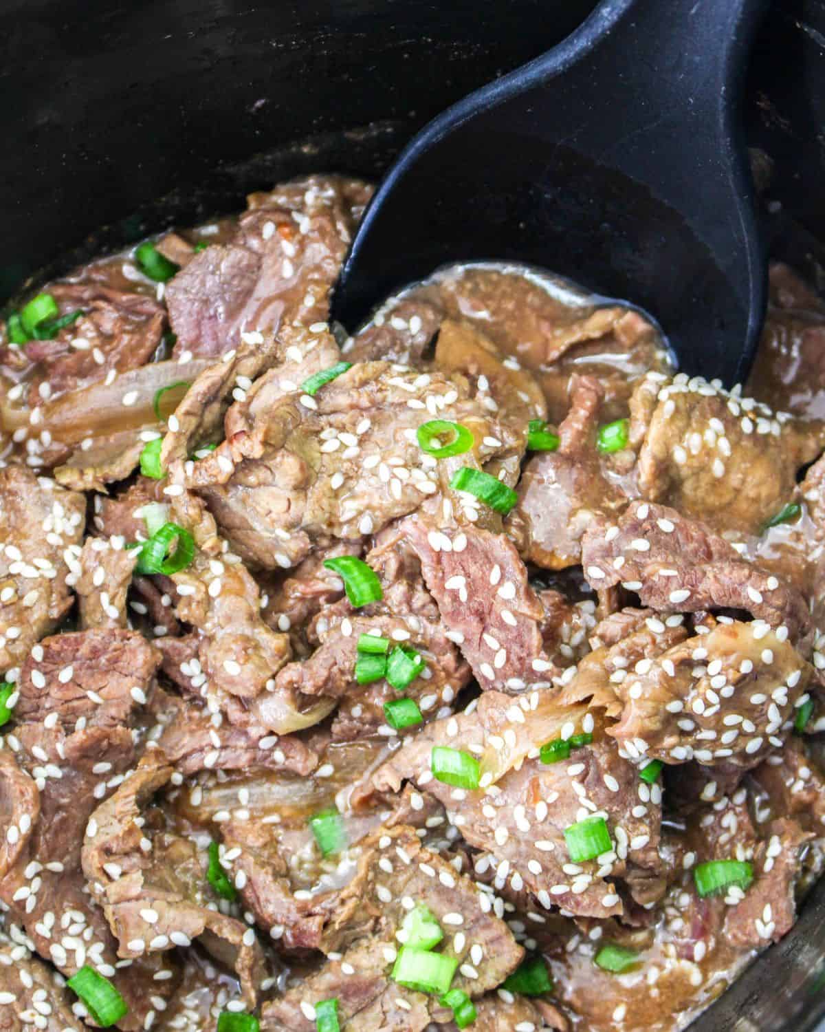 Korean beef made in the slow cooker topped with sesame seeds being picked up with a spoon.