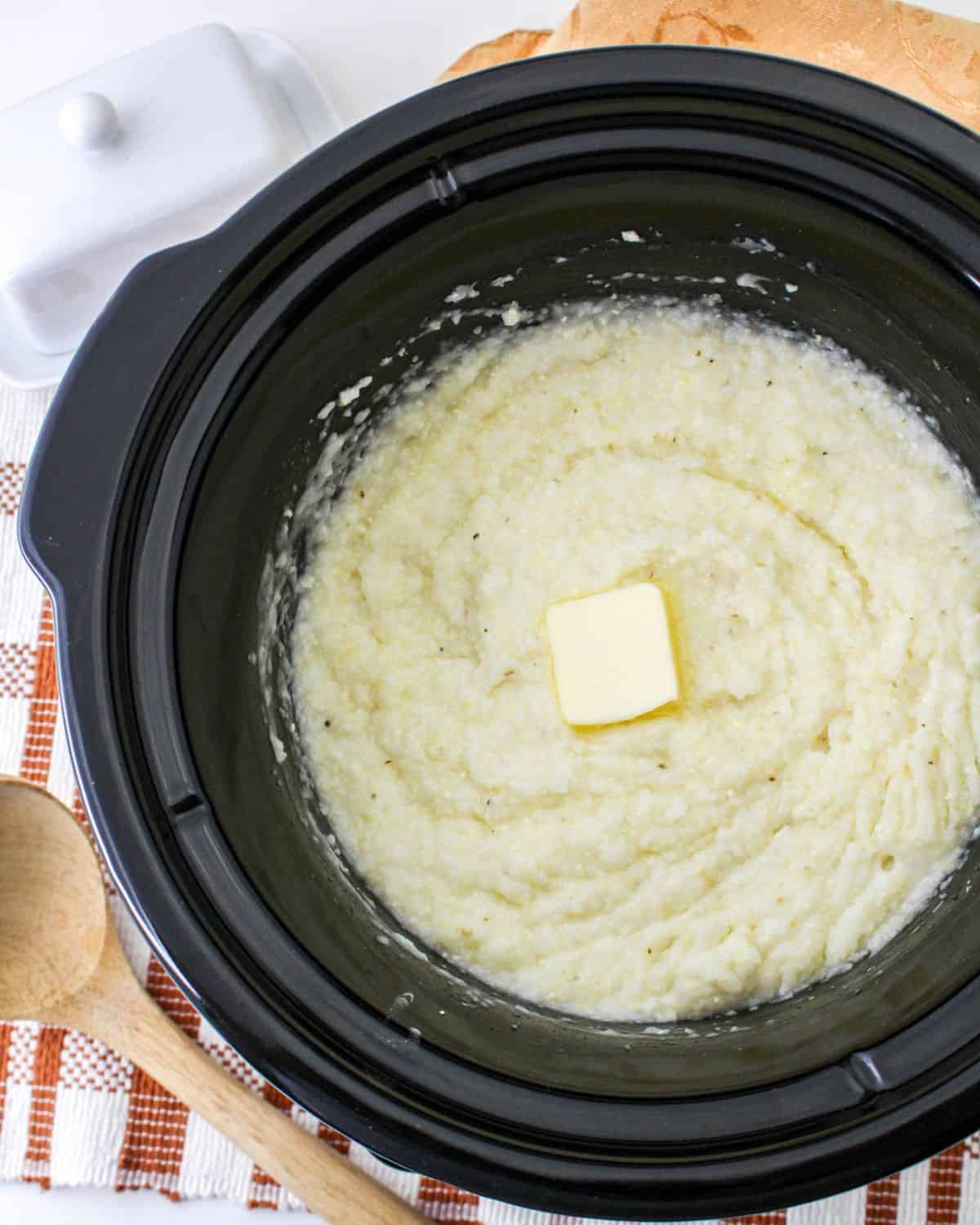 A slow cooker vessel with cooked grits topped with butter.