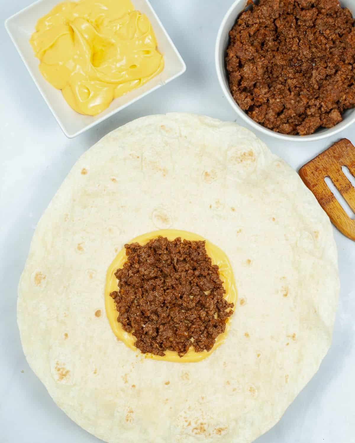 Process shot of a flour tortilla with nacho cheese and beef.