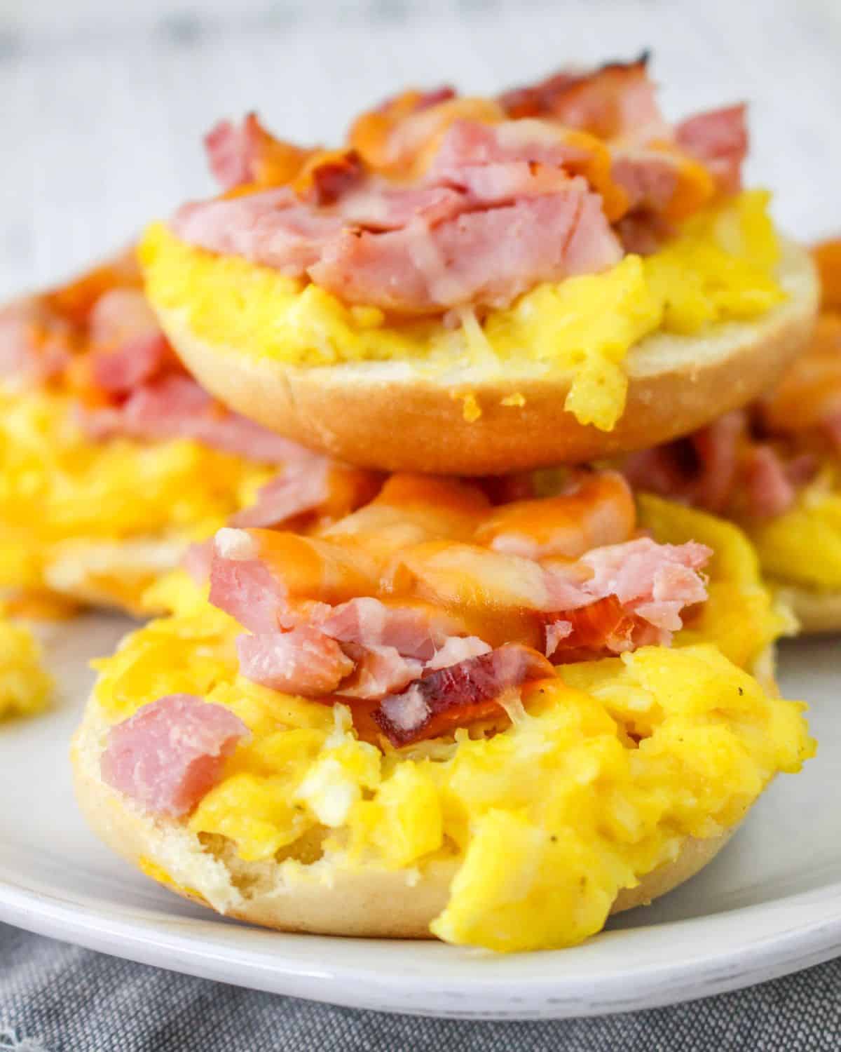 A stack of breakfast pizza bagels with ham and scrambled eggs.