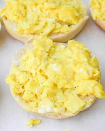 A bagel topped with scrambled eggs in a process photo of pizza egg bagels.