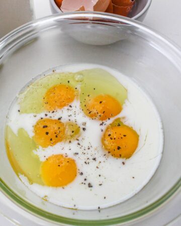 A clear mixing bowl with eggs and milk to make the eggs for breakfast pizzas