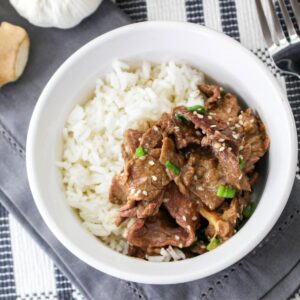 A white bowl with rice and cooked flank steak with Korean seasonings that was made in the slow cooker.