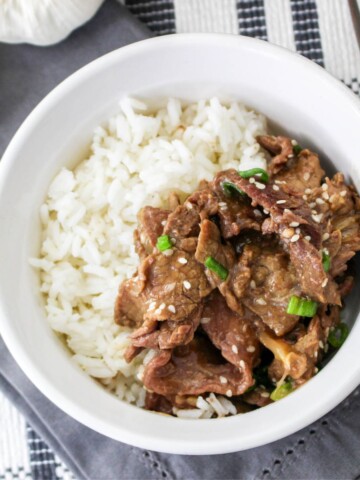 A white bowl with rice and cooked flank steak with Korean seasonings that was made in the slow cooker.