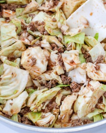 A saute pan with cooked ground beef and cabbage for a lazy cabbage casserole.