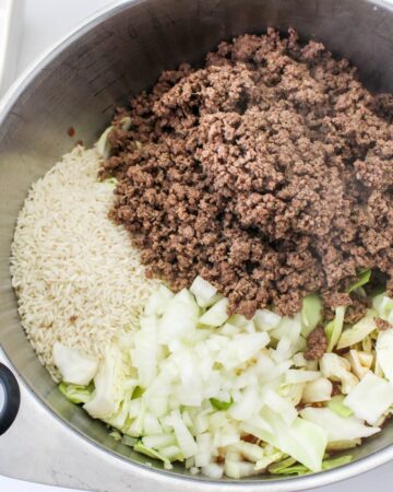 A large saute pan with cooked ground beef, rice, and chopped cabbage.