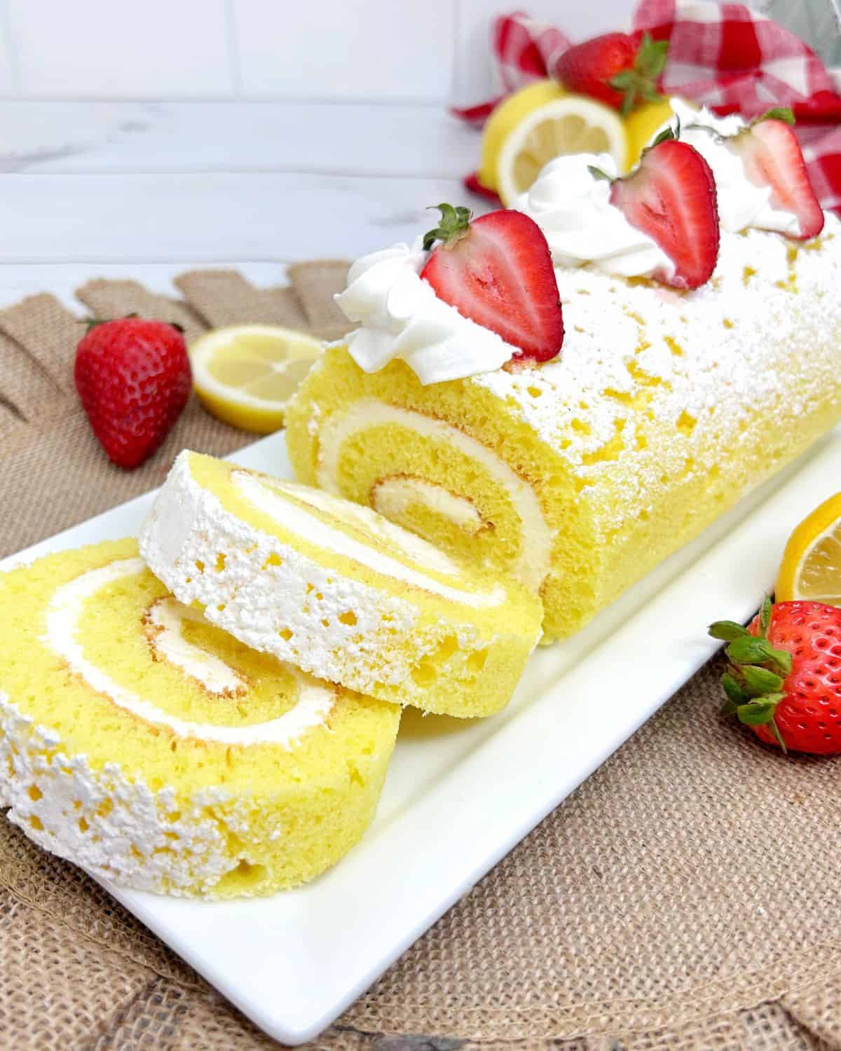 A sliced lemon roll cake topped with confectioner sugar and strawberries.