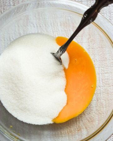 A glass bowl with egg yolks and sugar to make a pineapple upside down cake.