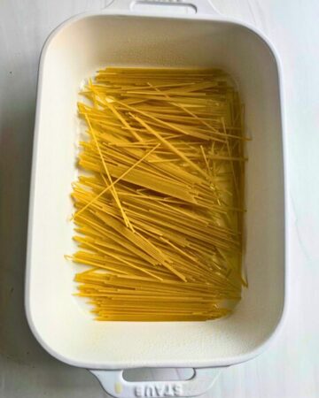 Casserole dish with water and broken spaghetti to make a baked spaghetti casserole.