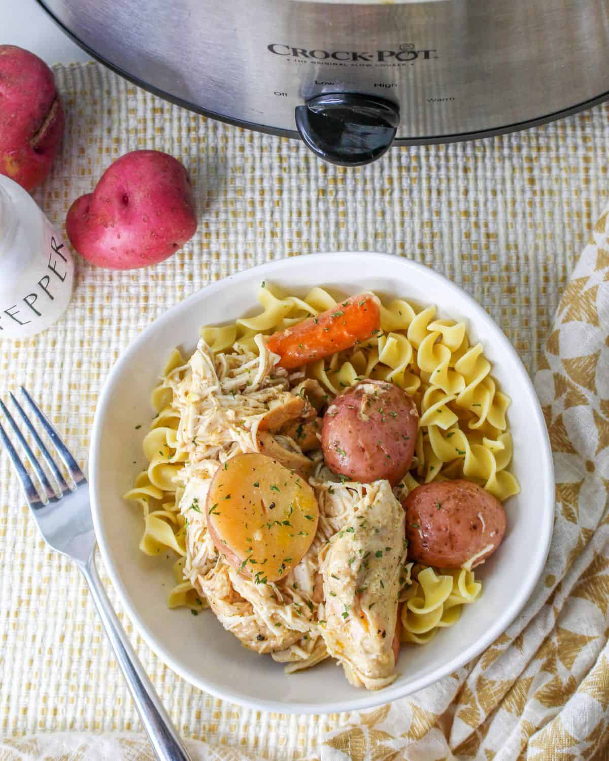 Crockpot Shredded chicken and potatoes with baby carrots served over noodles.