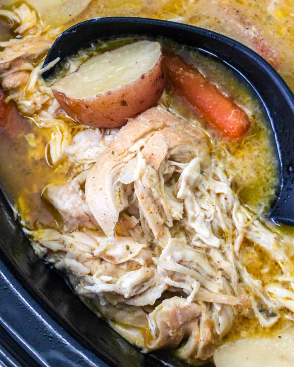 A slow cooker with shredded chicken, potatoes, and carrots to make an easy dinner.
