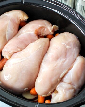 Chicken breasts on top of potatoes in a slow cooker to make chicken and potatoes.