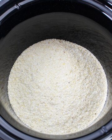 A slow cooker vessel with grits in the bottom.
